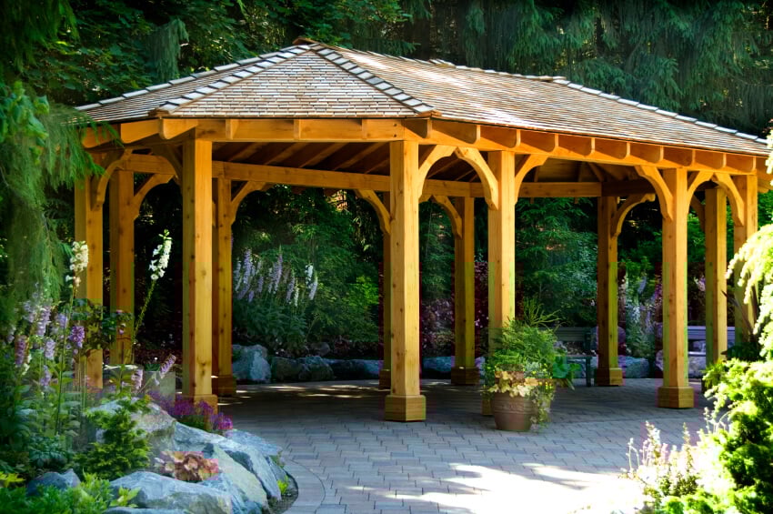 An open design ensures that there's plenty of space for a large gathering to move around without having a traffic jam at the entrance. This gazebo is tucked near a forest and surrounded by flowers.