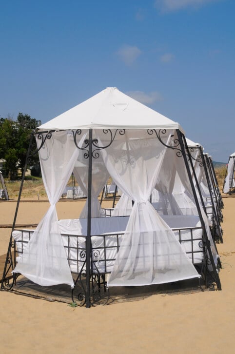 An aluminum gazebo with a canopy top and cushions formed to make a cozy bed-like structure. This gazebo is a luxurious way to relax on the beach and beat the summer heat.