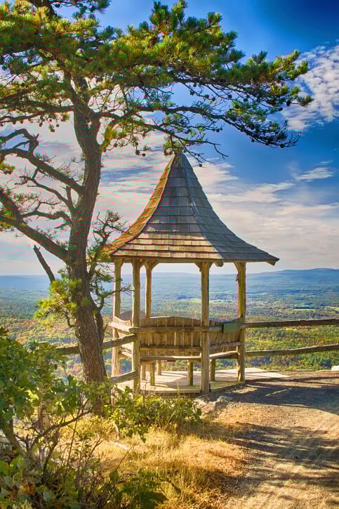 The incredibly tall roof of this small gazebo is shaped somewhat like a witch's hat. It is equipped with rustic benches on four sides.