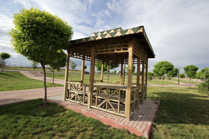 An eclectic square gazebo with clever details on the roof and a sunburst design on the sides. The structure is a nice spot to rest off the brick pathway.