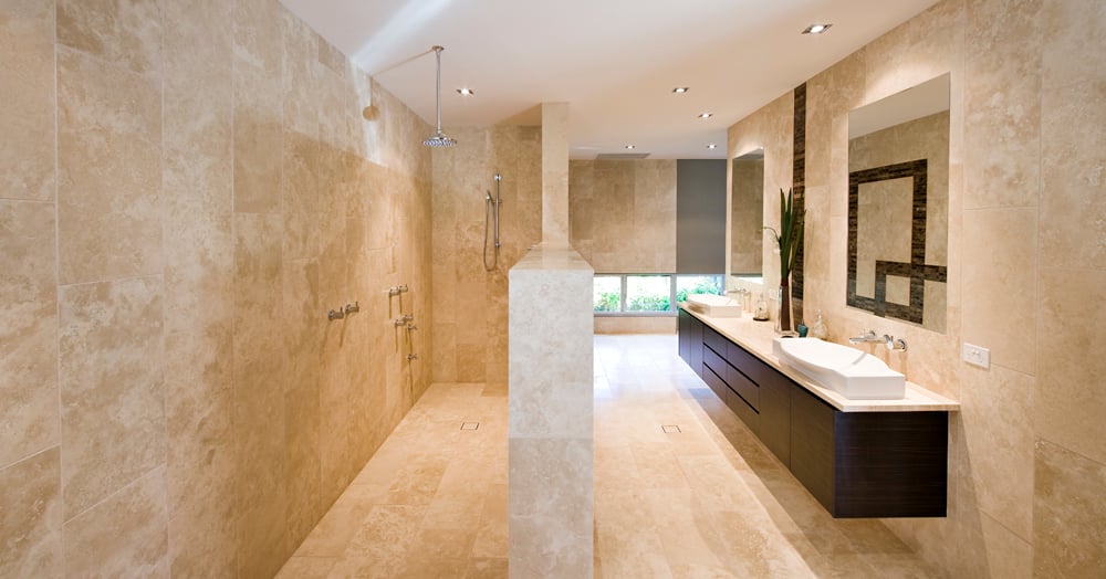 Gorgeous beige marble bathroom showcases an open shower area and a dark wood floating vanity with dual vessel sinks beneath frameless mirrors.