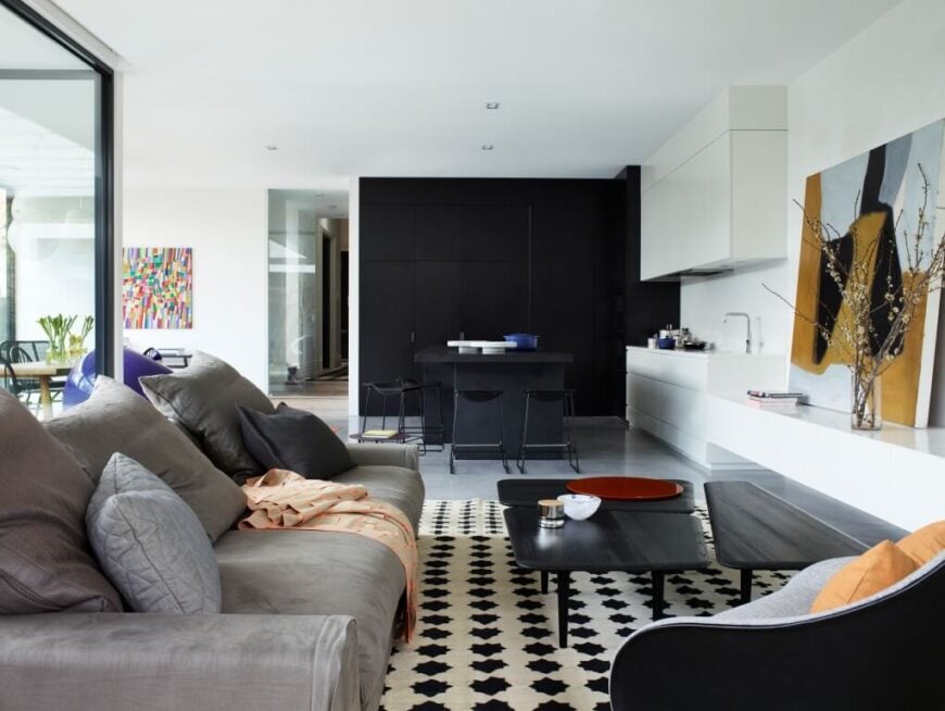 The living room is defined by a black and white area rug, with contemporary plush sofa and club chair facing over a novel rectangular dark wood coffee table, comprised of three complementary pieces.