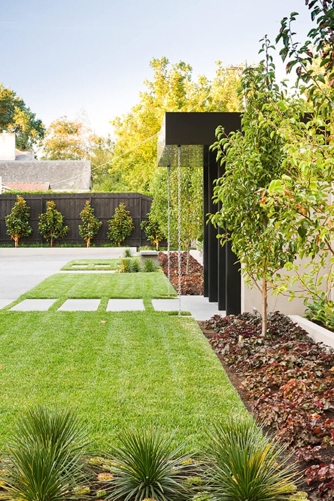 The entry gate, wrapped in black metal and flanked by expanses of manicured lawn, stands apart in stark simplicity. The sharp lines hint at the modern construction home ahead.