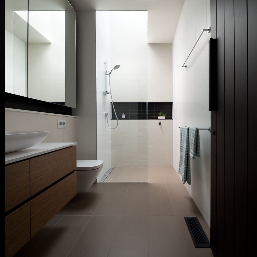 Primary bathroom features a wooden floating vanity topped with white marble and a vessel sink. It has a walk-in shower accented with a black subway tile backsplash. 