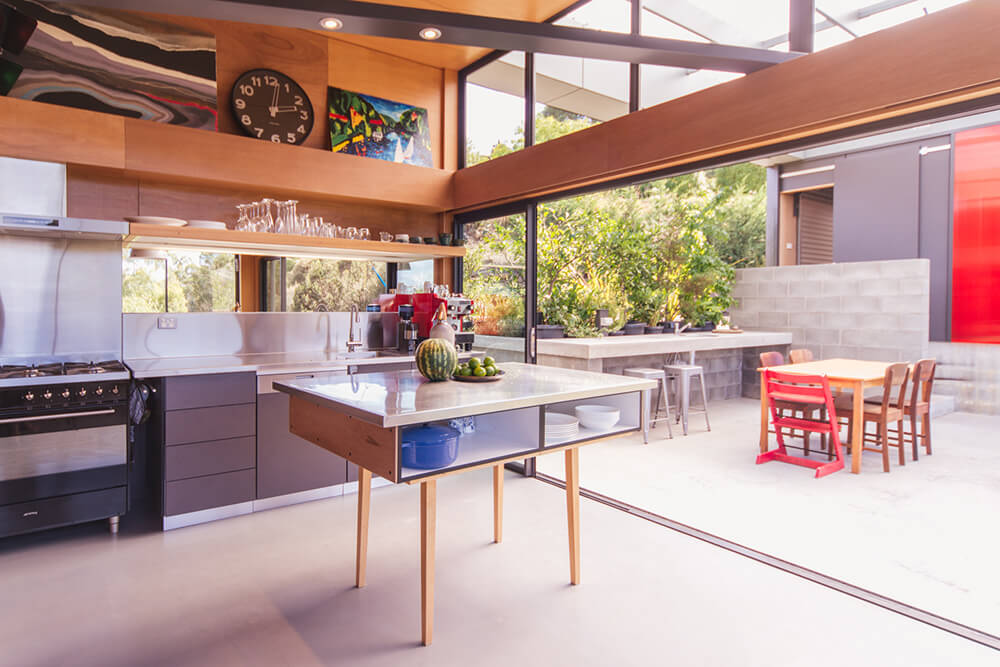 This kitchen boasts a modish counter and shelving. It is also connected to the outdoor dining area through the sliding glass door.