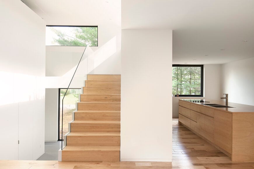 This image gives us a wonderful idea of how this house has been designed to be open and free flowing. The kitchen is spacious, and features a large island containing the sink and stove. From this one angle, we also get a view of the stairs leading up to the top level, and can even see the entryway as well.