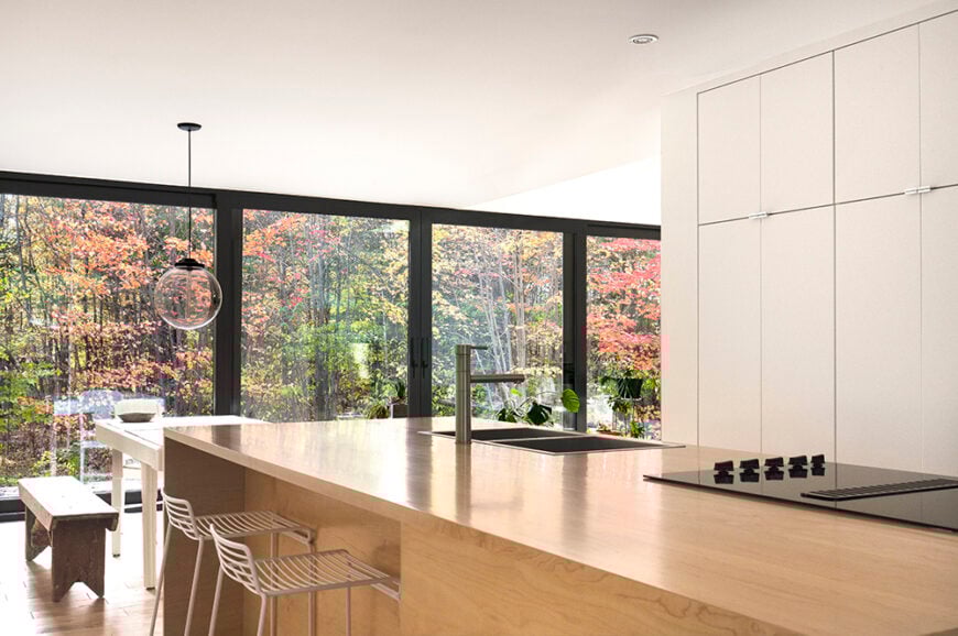 This shot from within the kitchen gives us a taste of some of the views that the homeowner will get to experience during the changing seasons. The light wood island matches that of the floor throughout the house, while an eat in extension is located near the edge of the island.