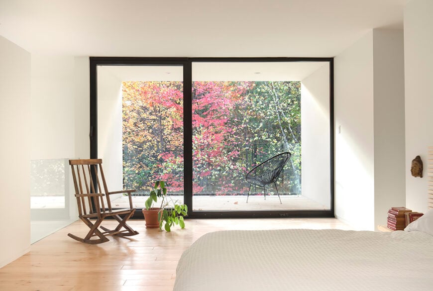 The bedroom is modest, and minimalistic. A rocking chair sits in the natural light from the glass slider door, and faces away from the opening to the lower level. The bed is across from the slider, which opens up to a small outdoor patio.