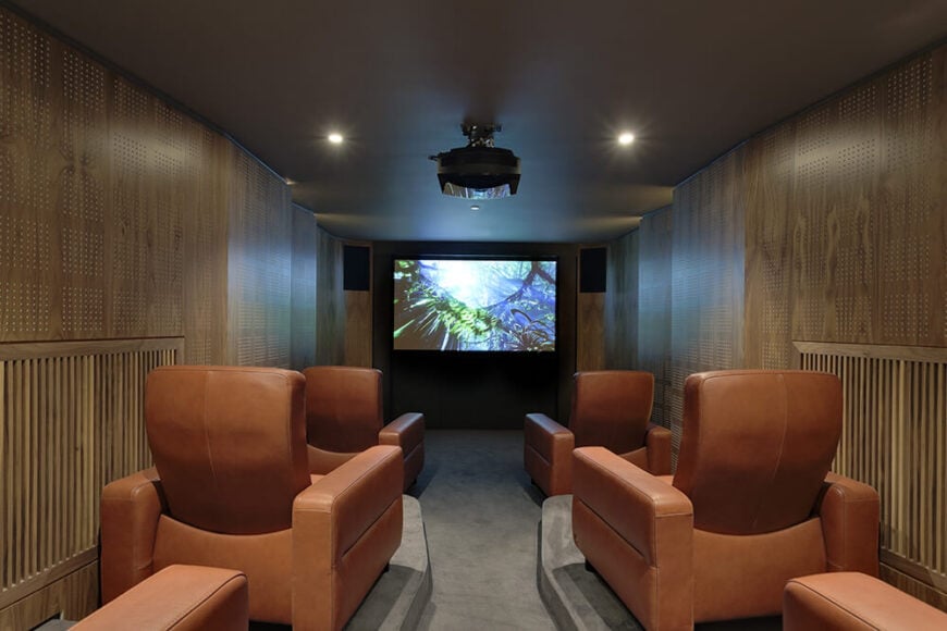 In the lower level, we see far more of the rich wood paneling. This is the cinema room, fitted with purpose built chairs for movie watching, as well as a projector and massive screen at the far end.