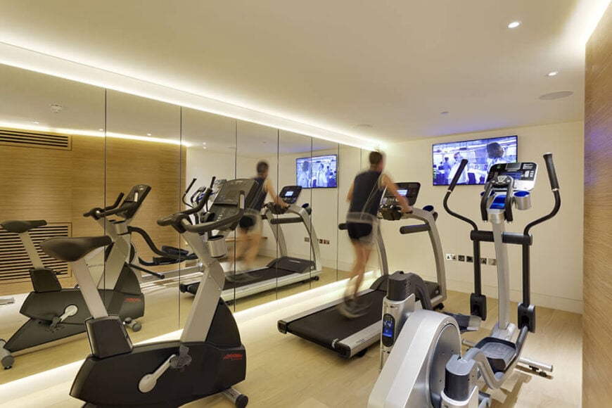 Next to the cinema room, we see the fully equipped home gym, featuring both natural wood paneling and full height, frameless mirrors bracketing the space.