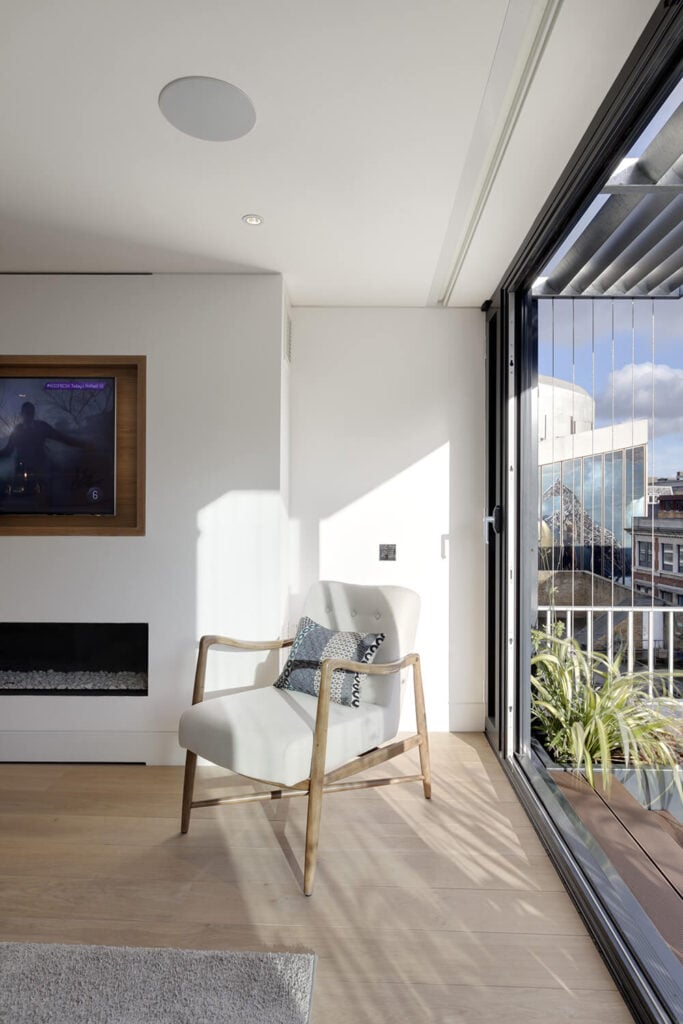 Next to the massive sliding glass door, we see one of many examples of elegantly crafted, neutral toned furniture in the home. This armchair features a minimalist wood frame and button tufted white leather upholstery.