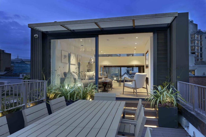 Moving outside the living room, we see one of the large terraces, filled with container gardens and a lengthy dining table. A small shaded awning hangs over the entryway.