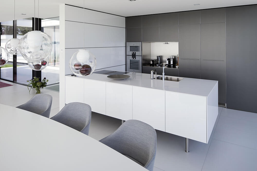 Modish kitchen with smooth white counters and countertops matching the white tiles flooring. The pendant lights look glamorous.