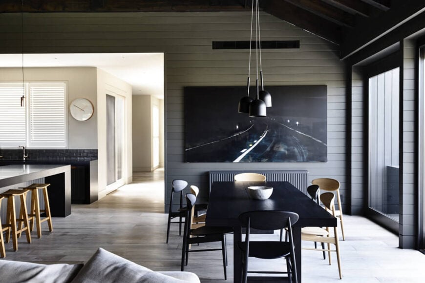The dining area centers on a large black wood table and assortment of natural wood chairs. From here, we can see the main hall leading to the bedrooms, drenched in sunlight.
