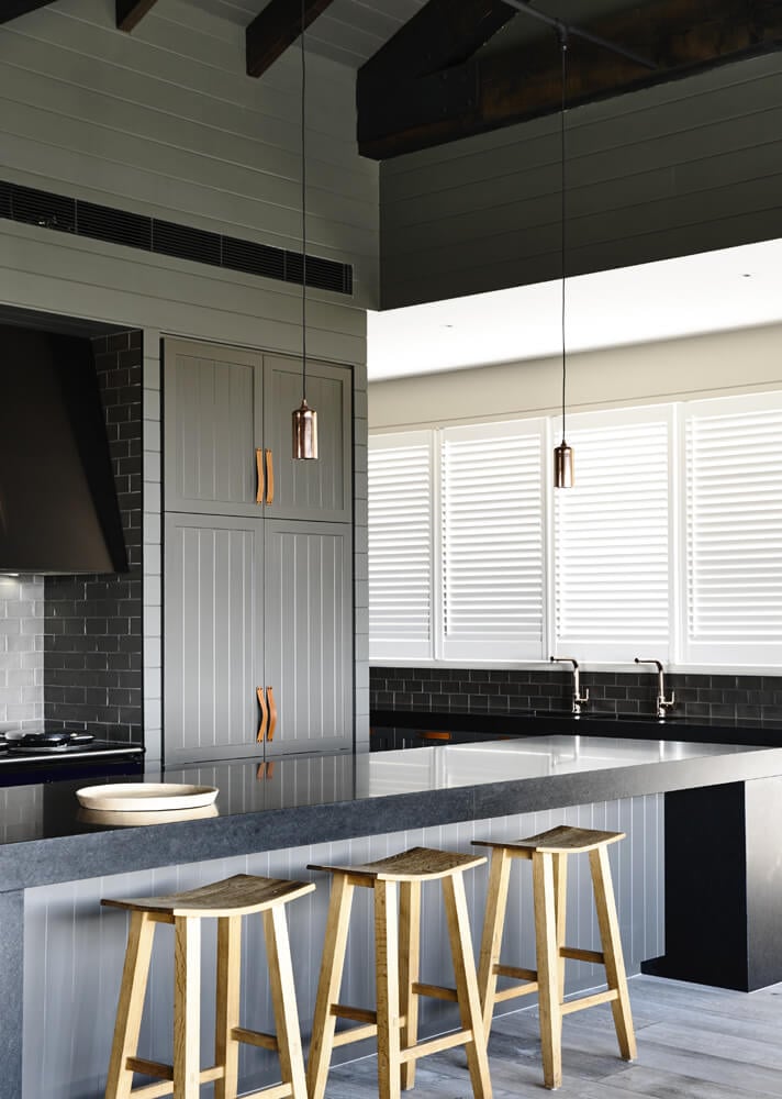 The kitchen is defined by this massive black slab topped island, with abundant space for in-kitchen dining. The sleek minimalism is buffered by grey subway tile walls.