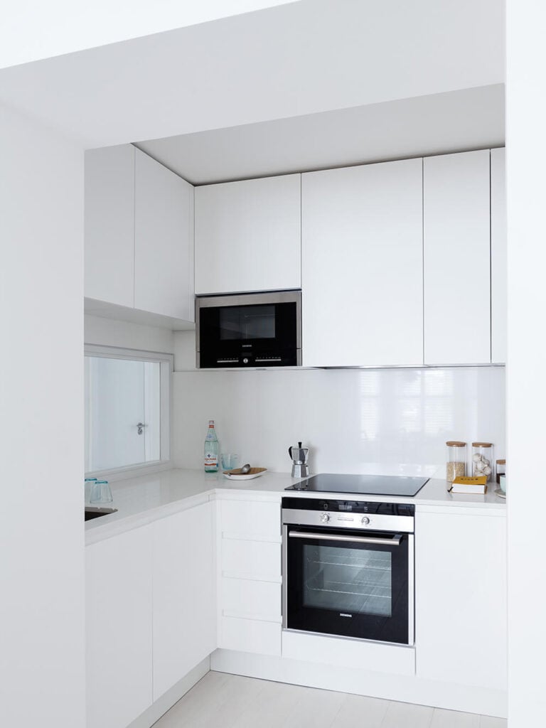 The kitchen is packed with storage options, courtesy of sleek white cabinetry that runs the full height of the space. A minimalist streak makes for a compelling, singular room.