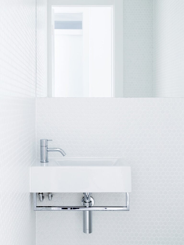 The bathroom boasts a simple, minimalist floating vanity in white and chrome, set against a honeycomb textured white wall.