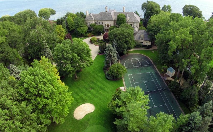 This is an aerial view of the property showcasing the golf area on one side and a large professional-size tennis court on the other side surrounded by tall trees and thick shrubs. Image courtesy of Toptenrealestatedeal.com.