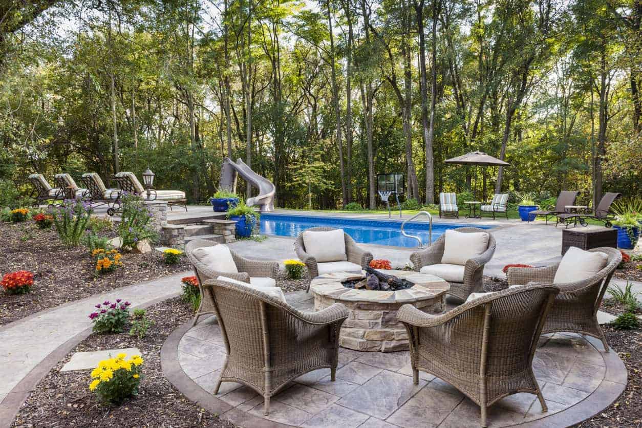 Stone above-ground round fire pit on patio next to a backyard swimming pool.