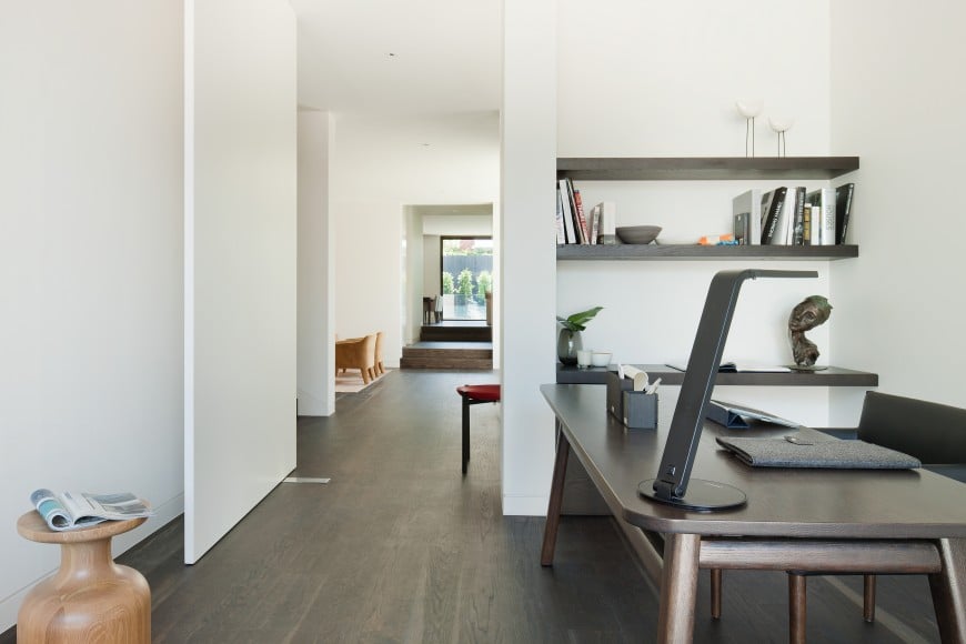 This home office offers a dark wood desk that complements with the floating shelves fixed against the white walls. 