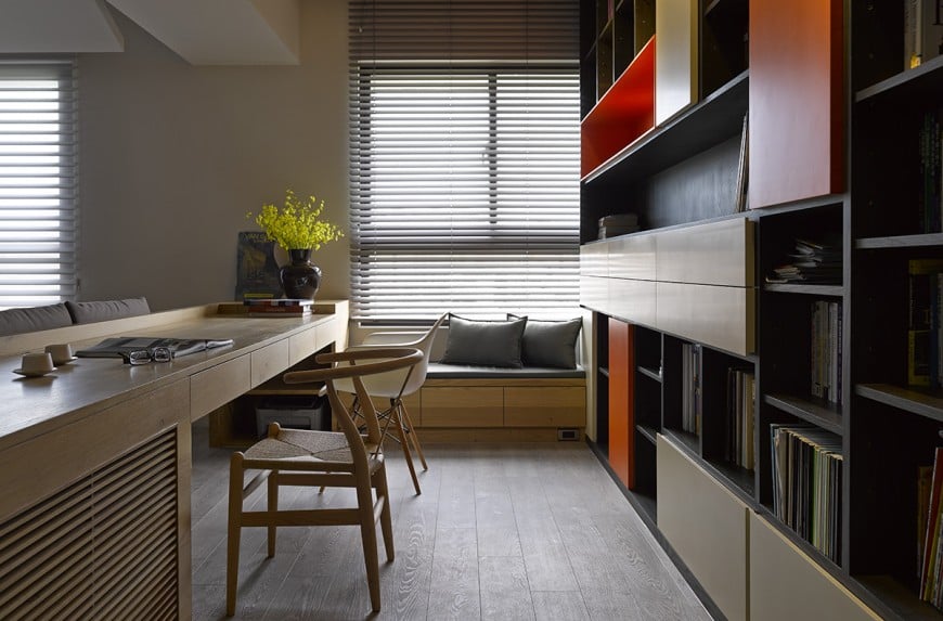Stylish home office featuring gorgeous open shelving and lengthy wooden desk paired with round back office chairs. It has a window seat nook topped with gray cushion and <a class=