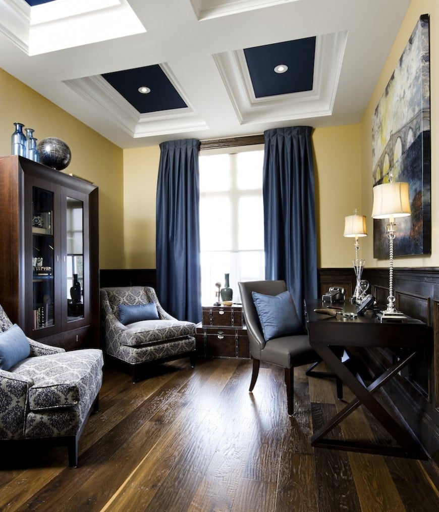 Elegant home office with seating area boasting a pair of blue patterned lounge chairs facing the dark wooden desk that's topped with classy table lamps.