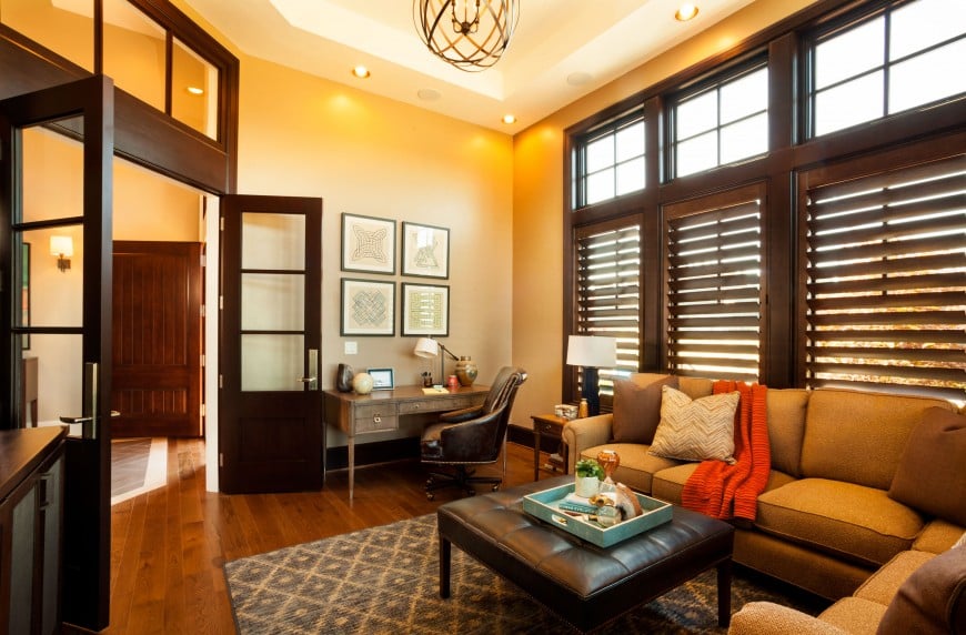 Warm living room offers a corner office decorated with wall arts that are mounted above the wooden desk with brown leather office chair.
