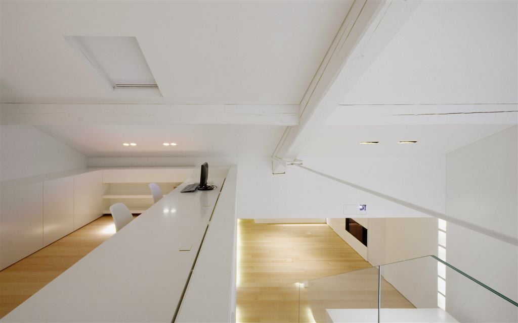 The elevated home office offers built-in storages and desk with a pair of office chairs. It has light hardwood flooring and shed ceiling fixed with recessed lighting.