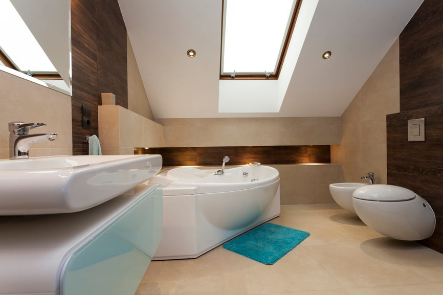 Modern primary bathroom boasts a floating sink vanity, a toilet and a bathtub over marble flooring. Walls are accented with dark wood that beautifully contrasts the white ceiling with inset skylight.