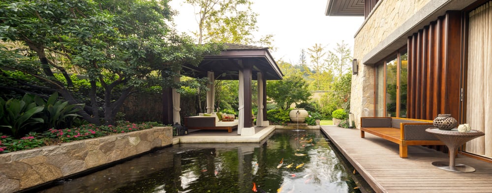 This deck features a comfortable seat with a side table. The pond full of colorful fishes looks glamorous.