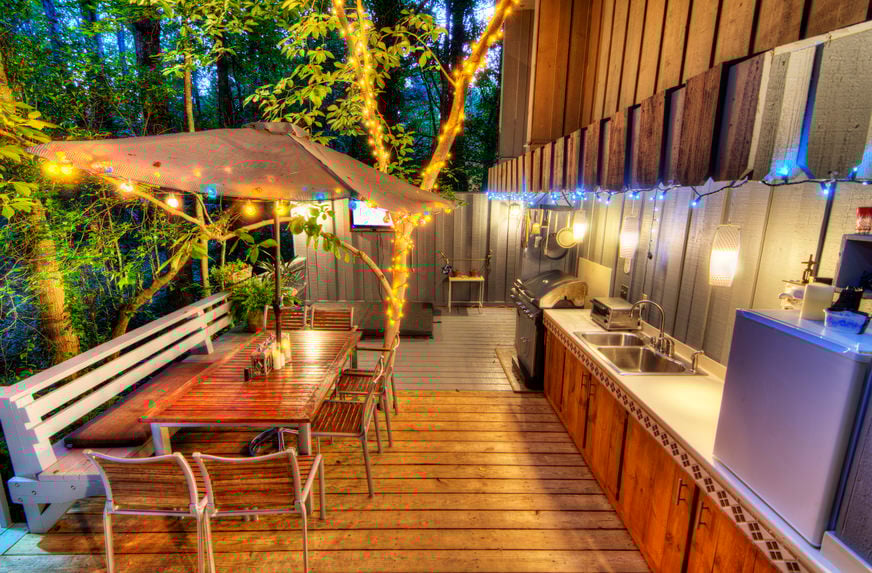 This deck features a complete set of outdoor kitchen and dining lighted by a romantic lights and surrounded by beautiful greens.