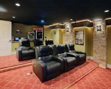 An eclectic type of media room with a carpeted floor and some bricked columns.