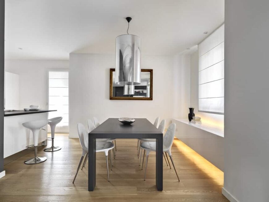 A dining area featuring modern dining table set and a bar area with modern bar stools surrounded by white walls.