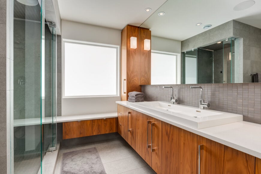 Contemporary primary bathroom with rich hardwood storage and dual sink vanity that matches the built-in window seat nook. 