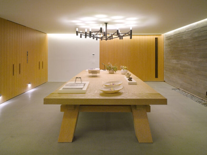 This dining room boasts a huge wooden table that complements with the mustard yellow shiplap wall and storage. It is lighted by an oversized chandelier that hung from the low white ceiling.