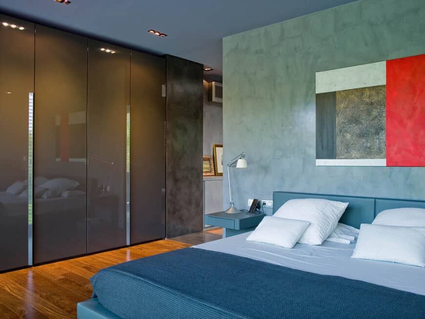 Contemporary primary bedroom with smoked glass wardrobe complementing the gray upholstered bed over hardwood flooring.