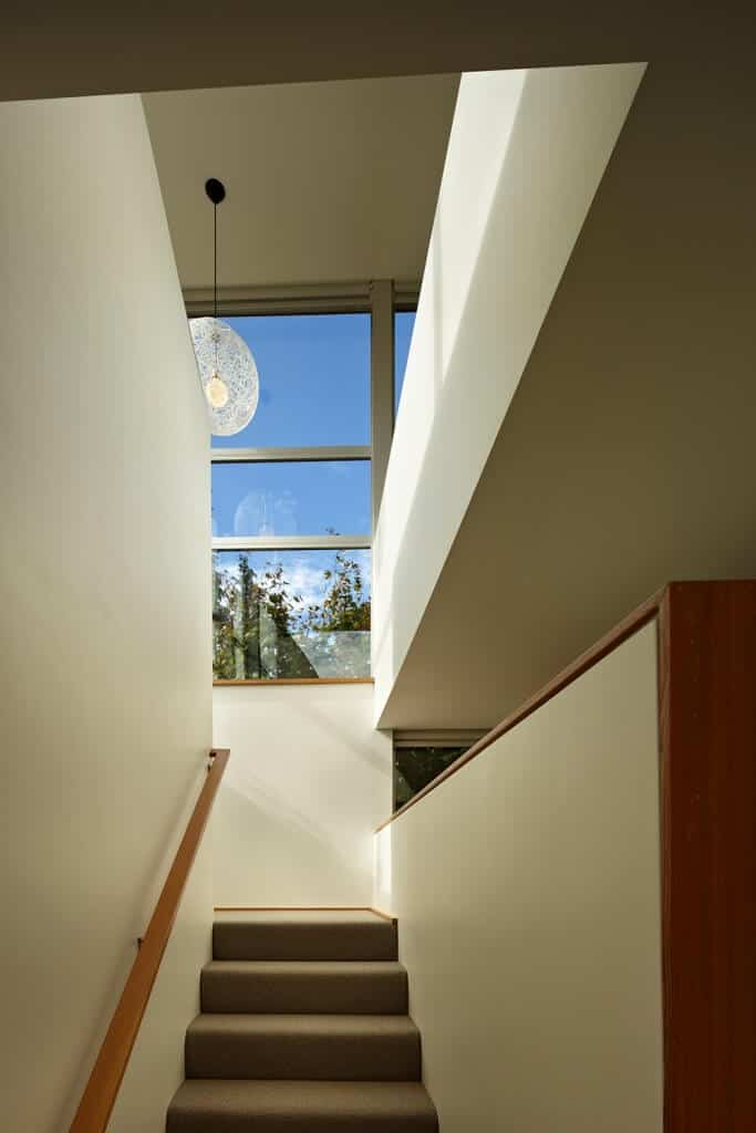 This home boasts a modish staircase surrounded by white walls. It features gray carpet floors and wooden handrail.