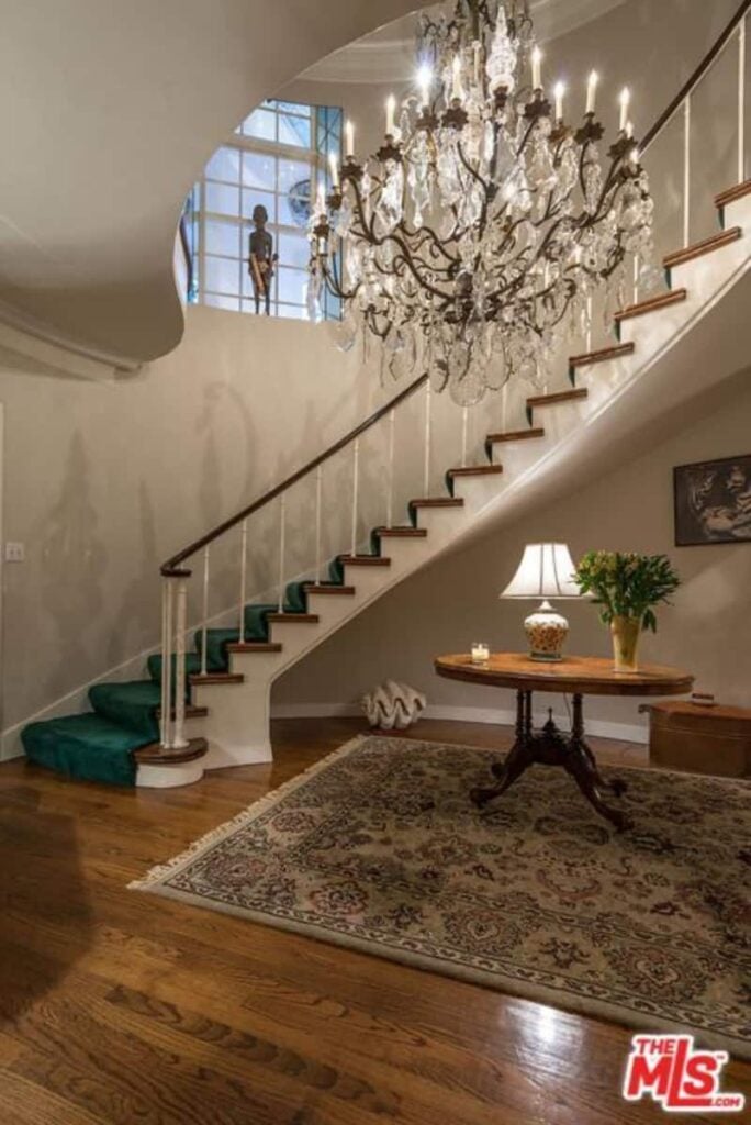 This home entry features a staircase with green walls lighted by a glamorous chandelier.