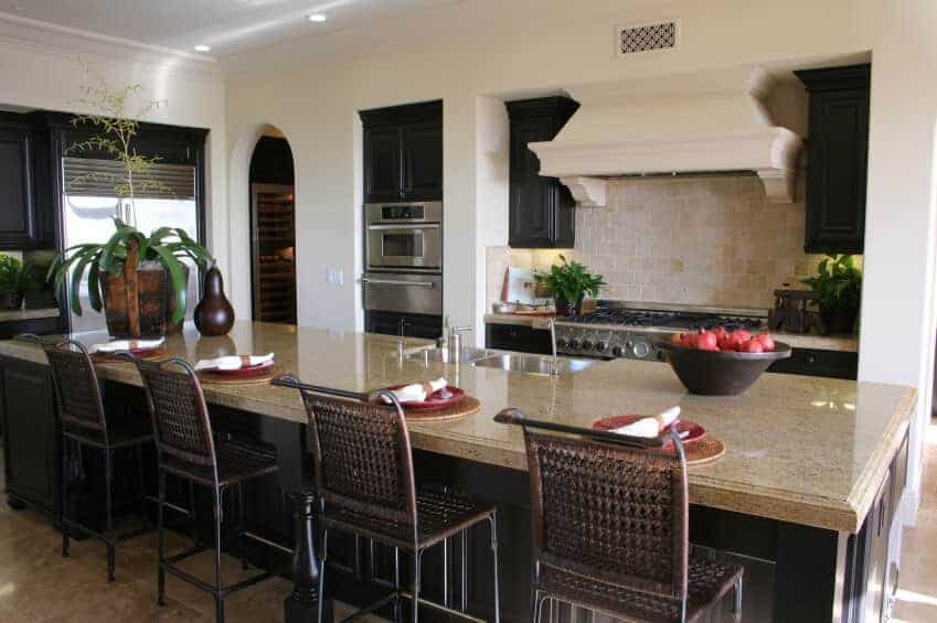 The beige countertops and beige backsplash of this Tropical-style kitchen is complemented by the lush potted plants of varying sizes. This also works well with the black wooden cabinetry that contrasts the white walls and white ceiling that has recessed lights.