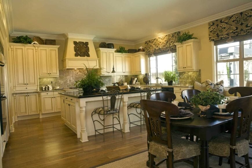 The beige vent hood of this Tropical-style kitchen is adorned with a large decorative artwork that somehow matches with the patterns of the window shades and the seat cushions of the wrought iron chairs paired with the kitchen island.