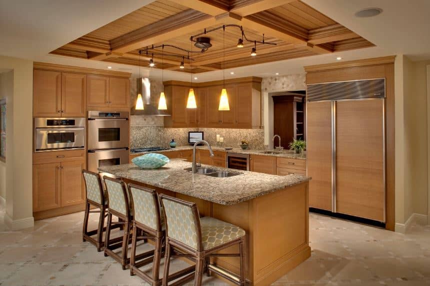 The elegant wooden coffered ceiling supports the four yellow pendant lights that casts a warm homey light on the wooden peninsula that also houses the stainless steel appliances. This is matched by the island that is paired with cushioned bamboo chairs.