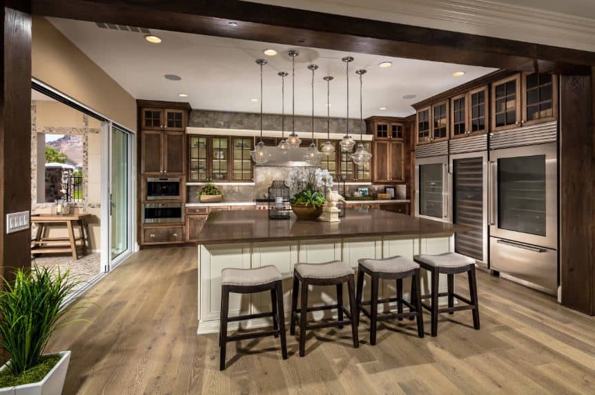 The hardwood flooring of this Tropical-style kitchen matches with the countertopof the large wooden kitchen island as well as the cabinetry of the kitchen peninsula on the far wall. Adjacent to this are the three large stainless steel appliances.