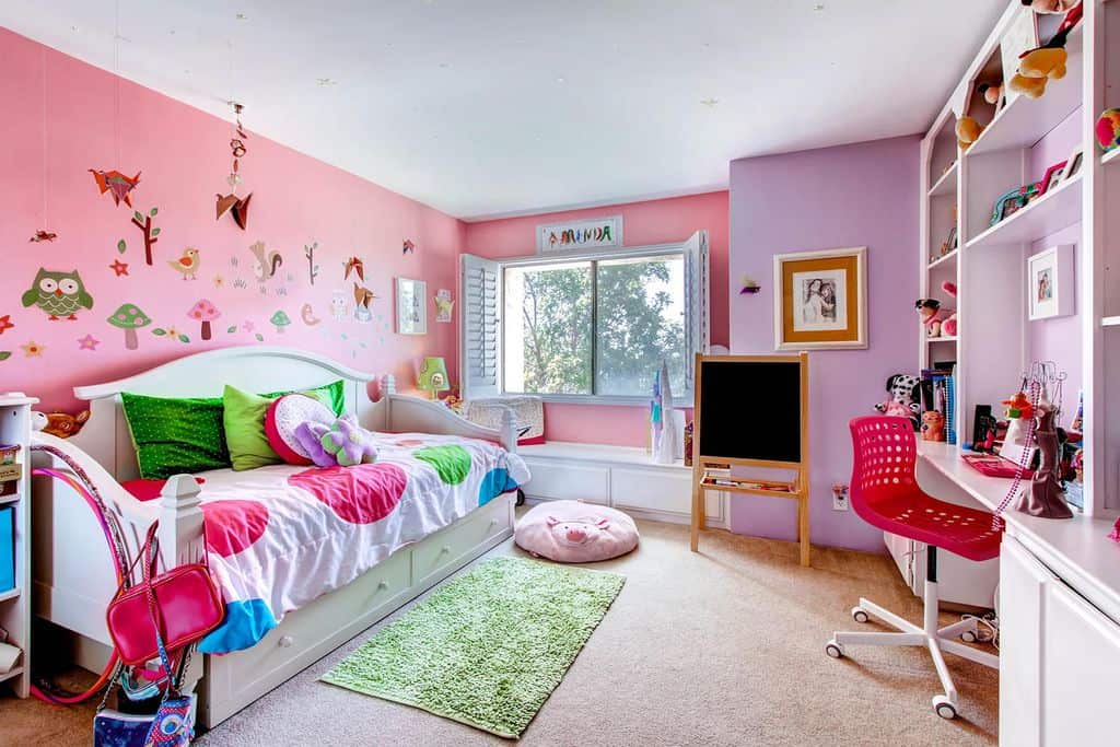 This girl's bedroom boasts pink and purple walls, along with carpet flooring and a rug. The study area looks perfect with the room's style.