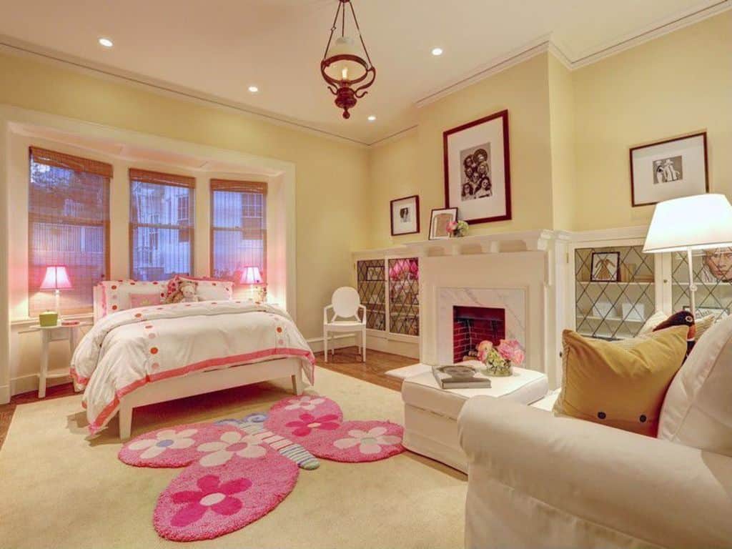 Large girl's bedroom with a fireplace on the side. the rugs look cute and lovely. The lights are very attractive as well.