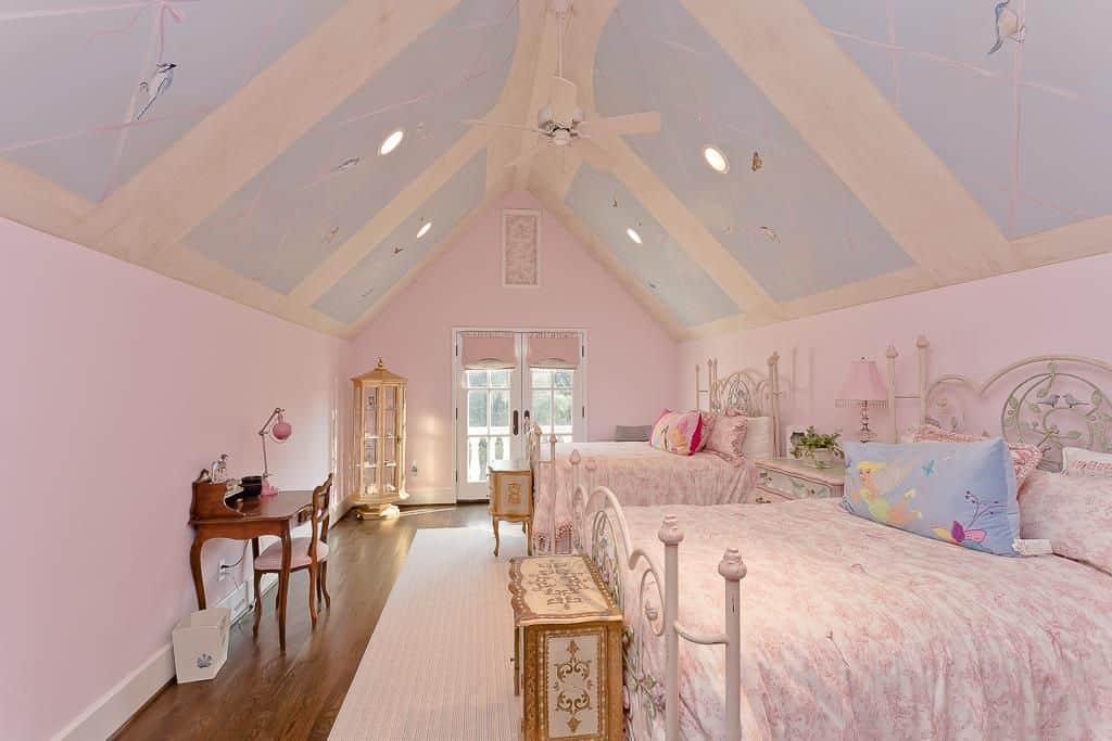 Large girls bedroom featuring pink walls and a stunning vaulted ceiling. The pink walls match perfectly together with the pink beds and table.
