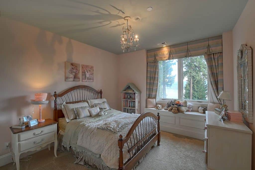 An elegant girl's bedroom with a carpet flooring and gray ceiling lighted by a small chandelier.