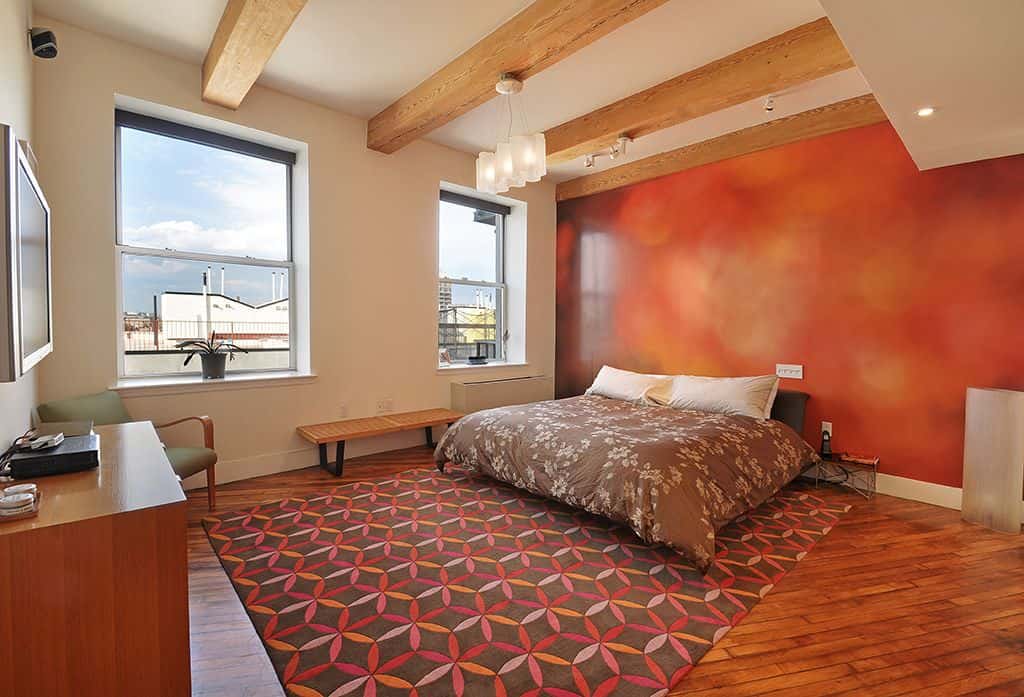 Glass pendant lights hang over the platform bed facing the wooden cabinet with a green armchair on the side. It sits on an eye-catching patterned rug over the hardwood flooring.