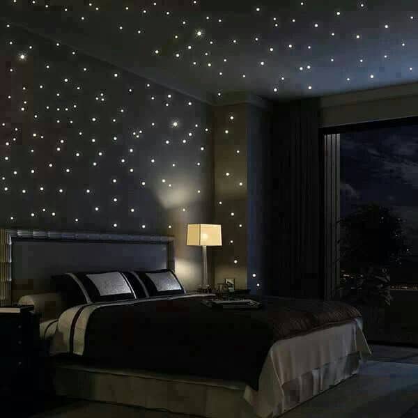 This primary bedroom features a skirted bed and dark wood nightstands topped with sleek table lamps. It is illuminated by recessed lights resembling stars on a night sky.