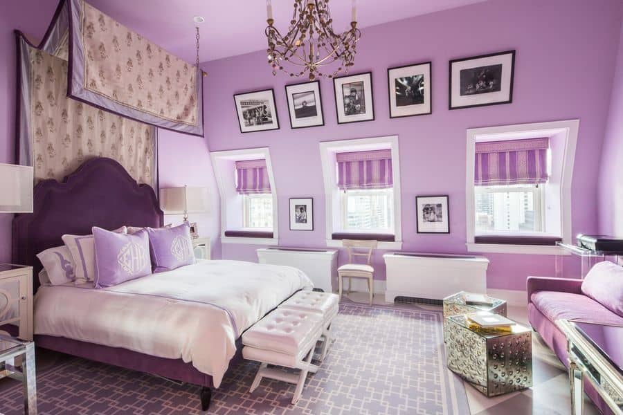 Purple primary bedroom decorated with photo gallery and a fabulous chandelier that hung over the white tufted stools sitting in front of the upholstered bed. There's a seating area on the side offering a cozy sofa and a pair of chrome coffee tables.