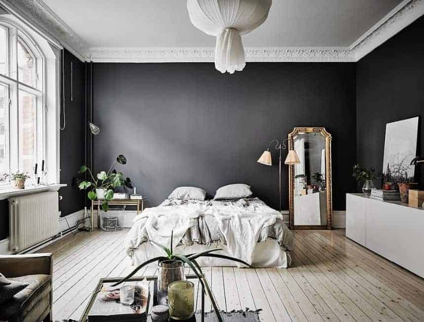 This Scandinavian-Style primary bedroom boasts elegant black walls surrounding the room. The hardwood flooring adds charm to the area. The ceiling looks stunning as well.